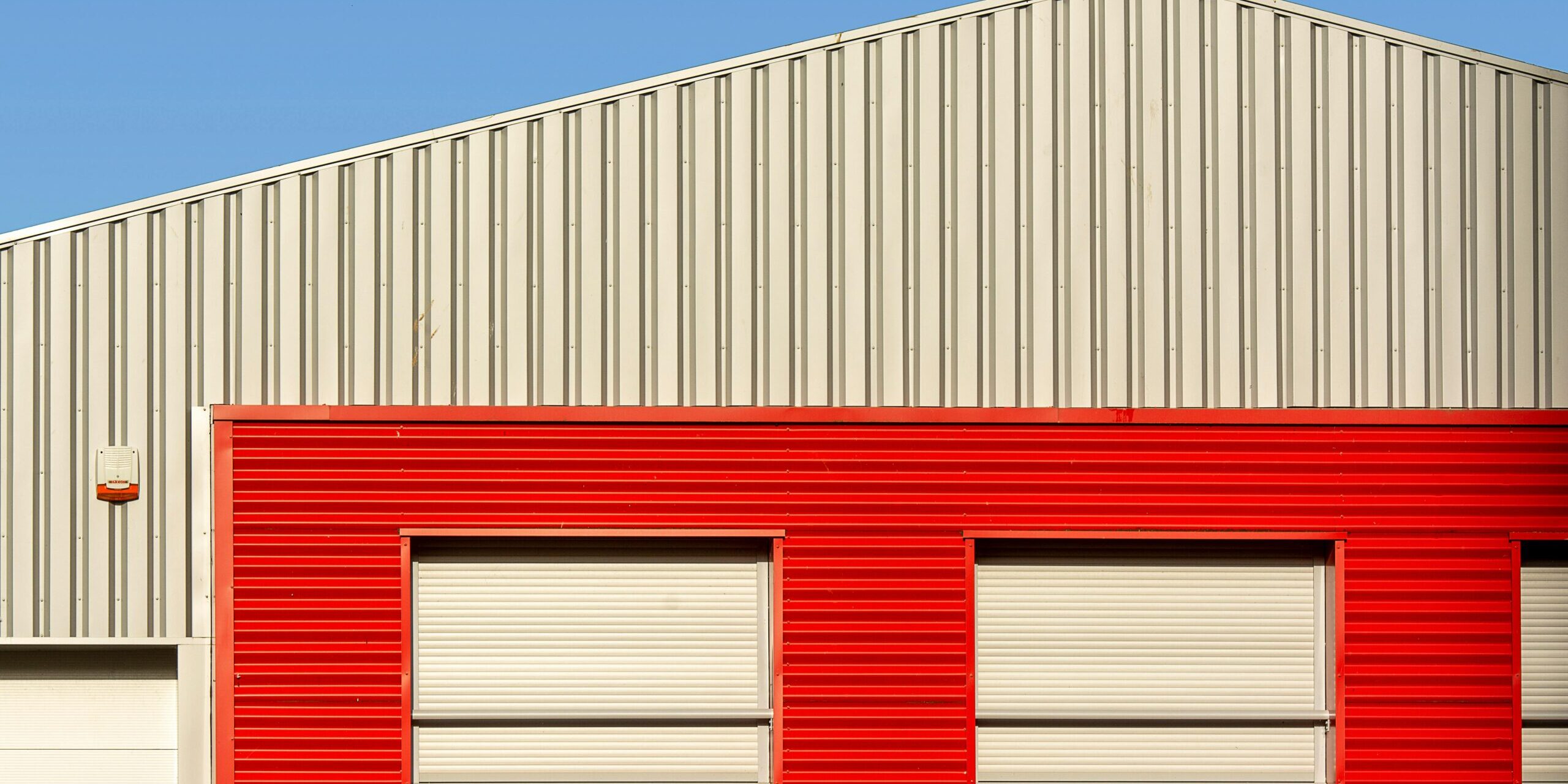 A modern industrial building with a red facade and A modern industrial building with a red facade and a seagull perched on the roof under clear blue skies.