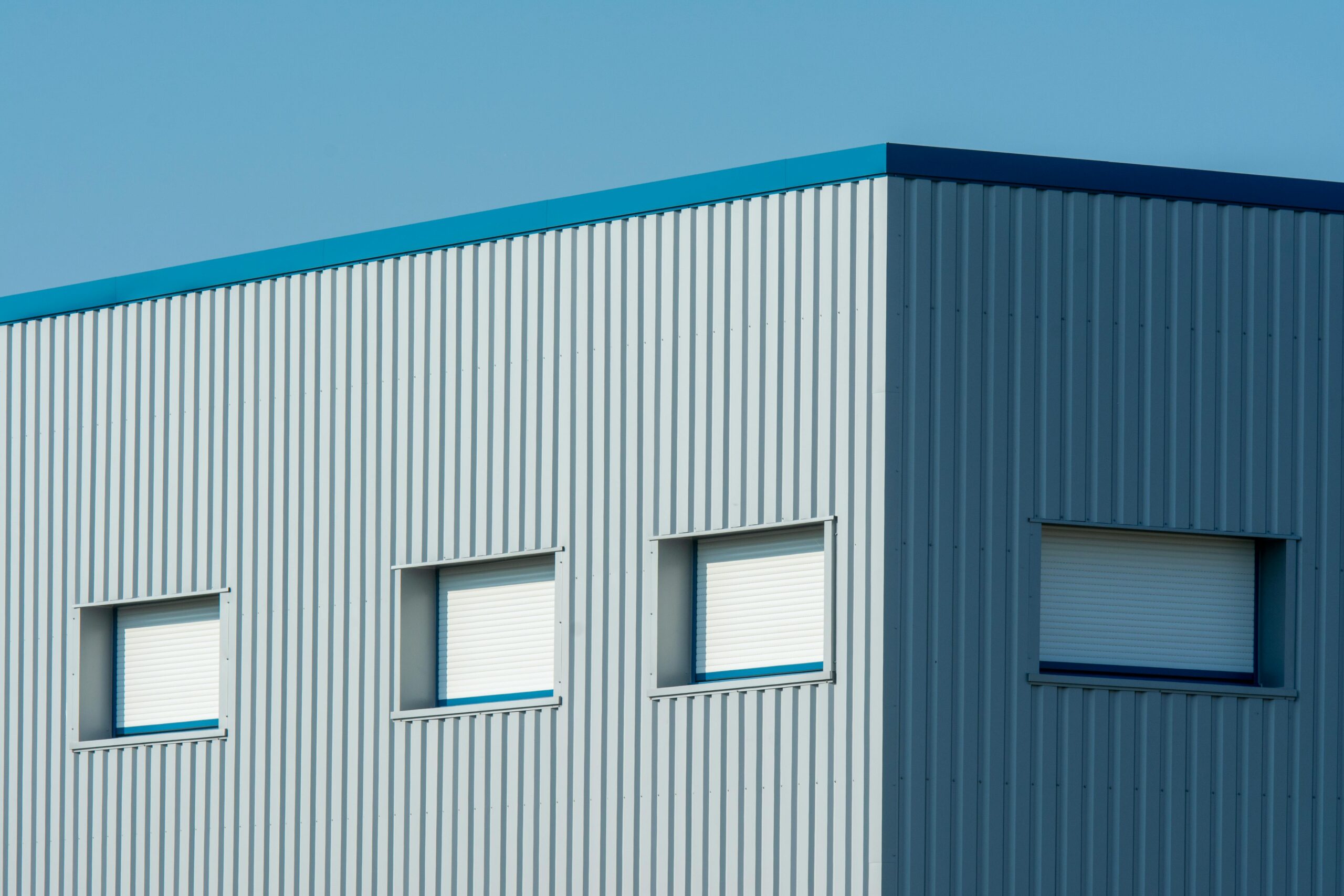 A sleek industrial building with a corrugated metal facade featuring roller blinds and sandwich panels.