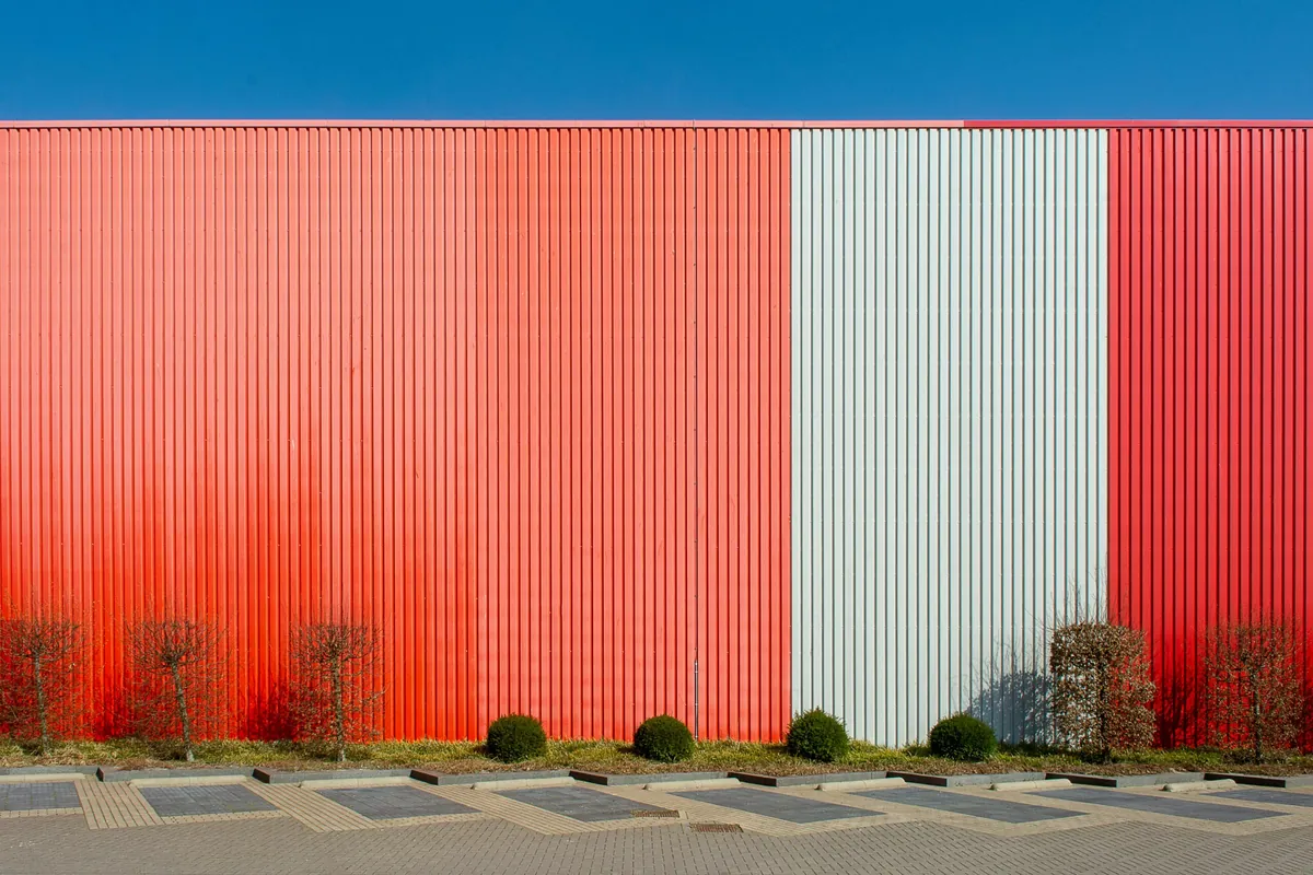 A vibrant red and white paneled wall of an industrial building with clear blue sky.