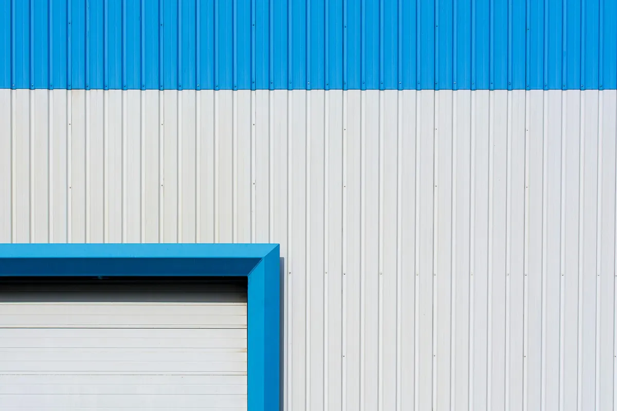 Abstract view of a blue and white industrial building wall with roller door, highlighting geometric patterns and colors.
