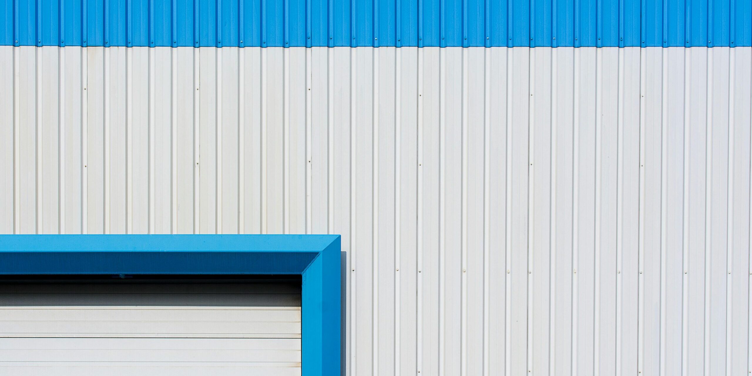 Abstract view of a blue and white industrial building wall with roller door, highlighting geometric patterns and colors.