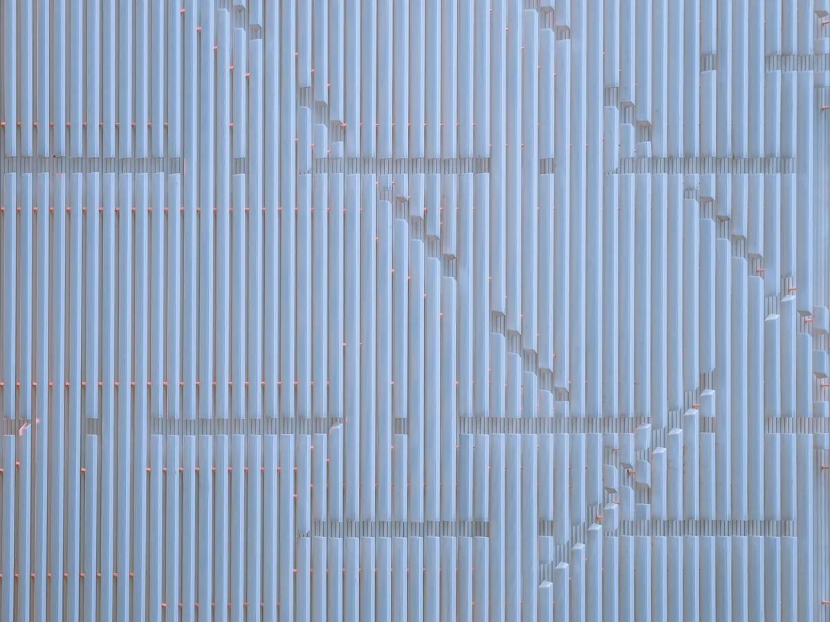 Hyper-realistic photography contrasting a small, hand-held sample piece of an aluminum sandwich panel with a large, full-sized production panel. The sample piece is on a workbench with design blueprints, while the full panel is in the background, ready for shipment. Soft, focused lighting on the sample, with the larger panel slightly blurred. Clean composition, no text, no brand logos. Illustrate the difference between prototyping and bulk orders from aluminum sandwich suppliers.