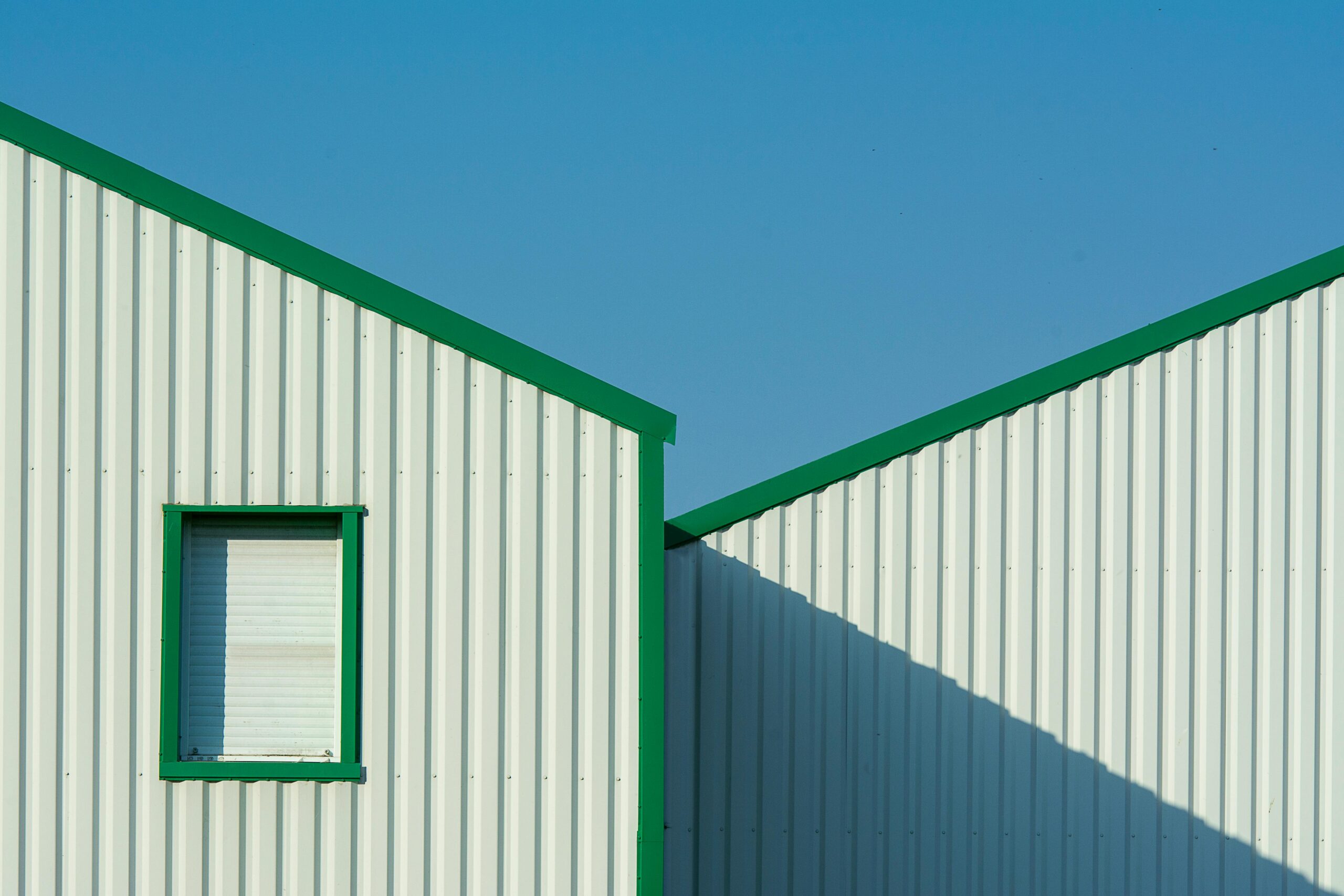 Minimalist building exterior with green accents under a clear blue sky.