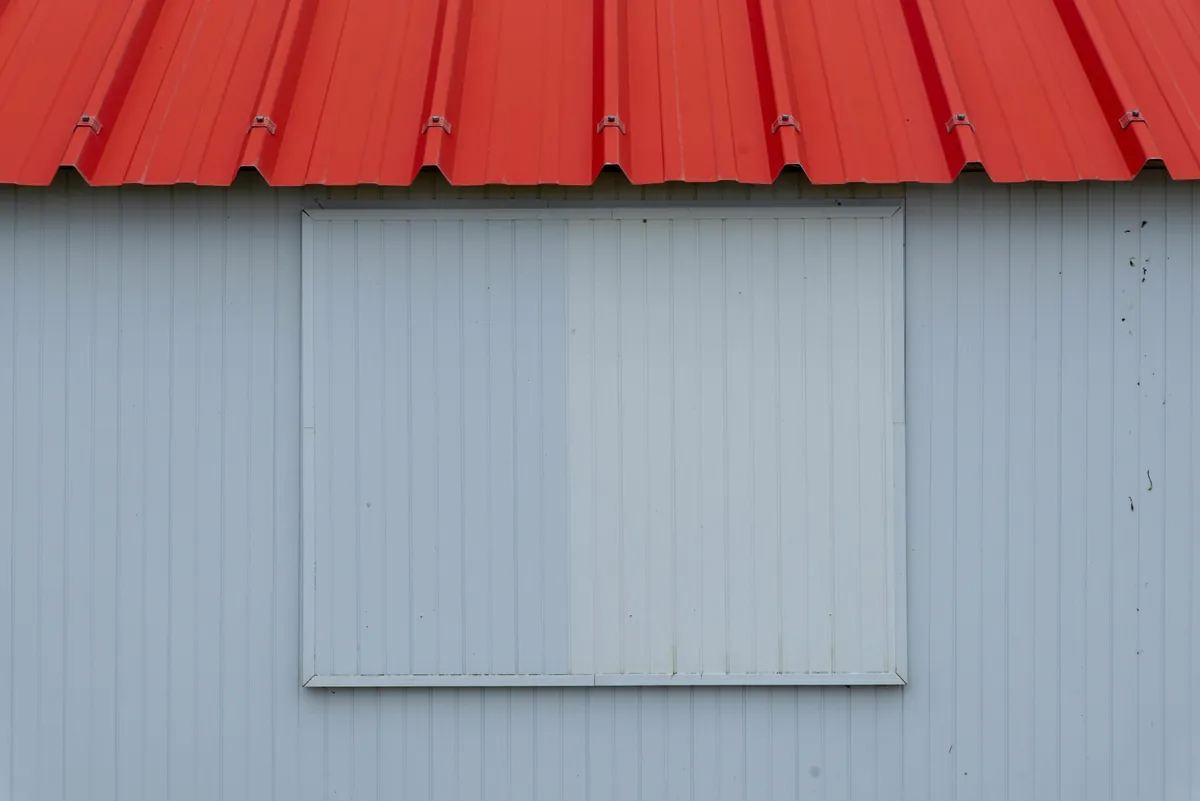 Minimalist image of a red metal roof with blue-grey corrugated panel wall.