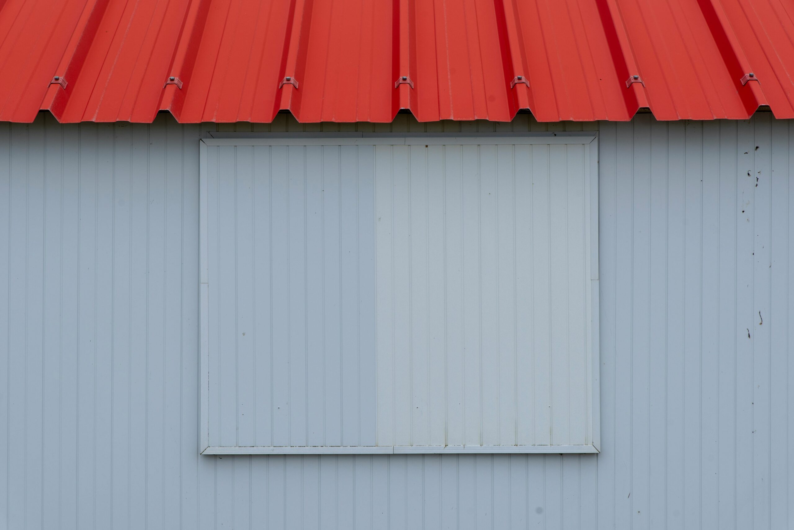 Minimalist image of a red metal roof with blue-grey corrugated panel wall.