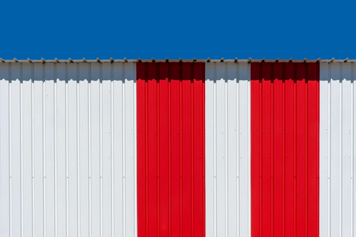 Minimalist photo of a red and white striped metal wall with a bright blue sky.
