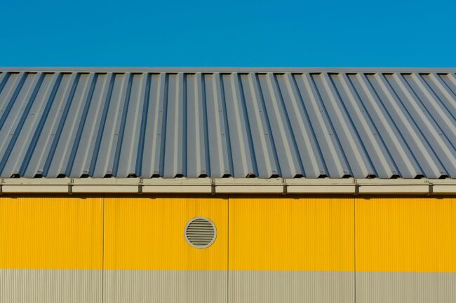 Modern industrial building’s yellow facade with me Modern industrial building's yellow facade with metal roof against clear blue sky.
