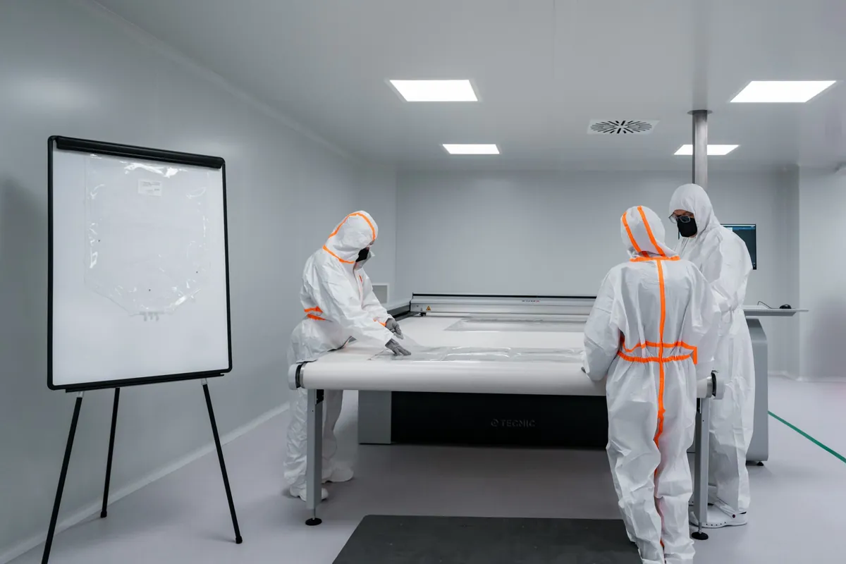 Workers in protective suits work in a cleanroom.